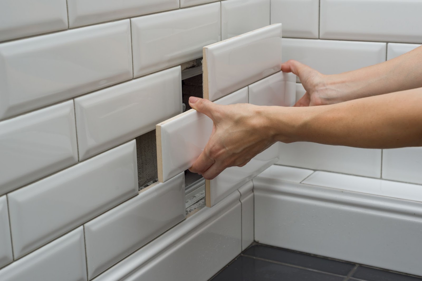 hands installing white rectangular stacked shower wall tiles