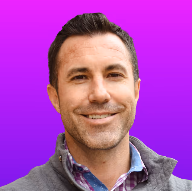 Smiling man with short dark hair wearing a gray jacket and a checkered shirt against a purple gradient background.