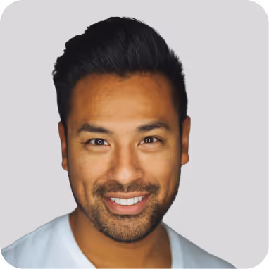 Smiling woman with curly hair, glasses, and a heart-shaped necklace wearing a blue top.