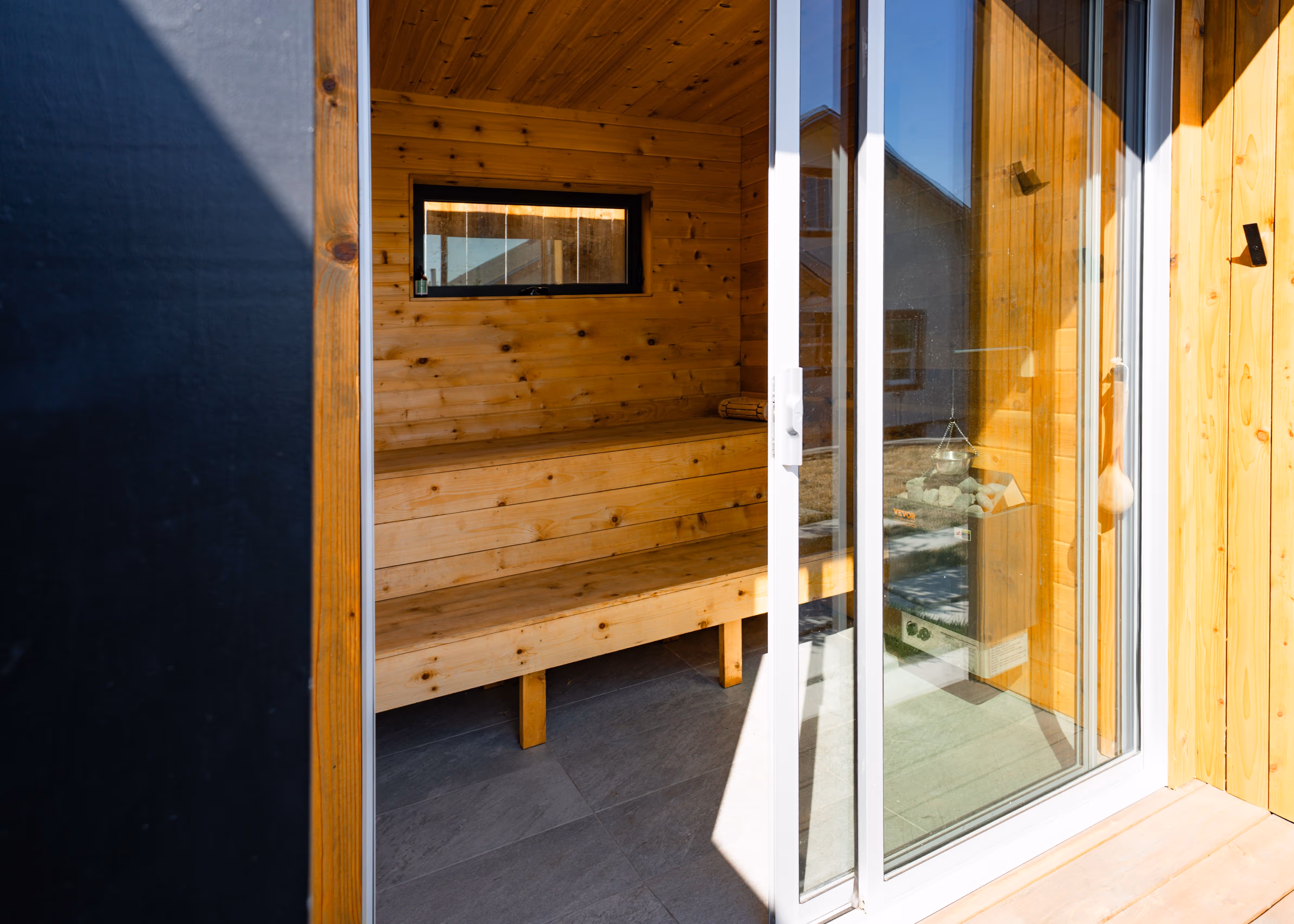 Interior view of a wooden sauna with a glass sliding door and bench seating.