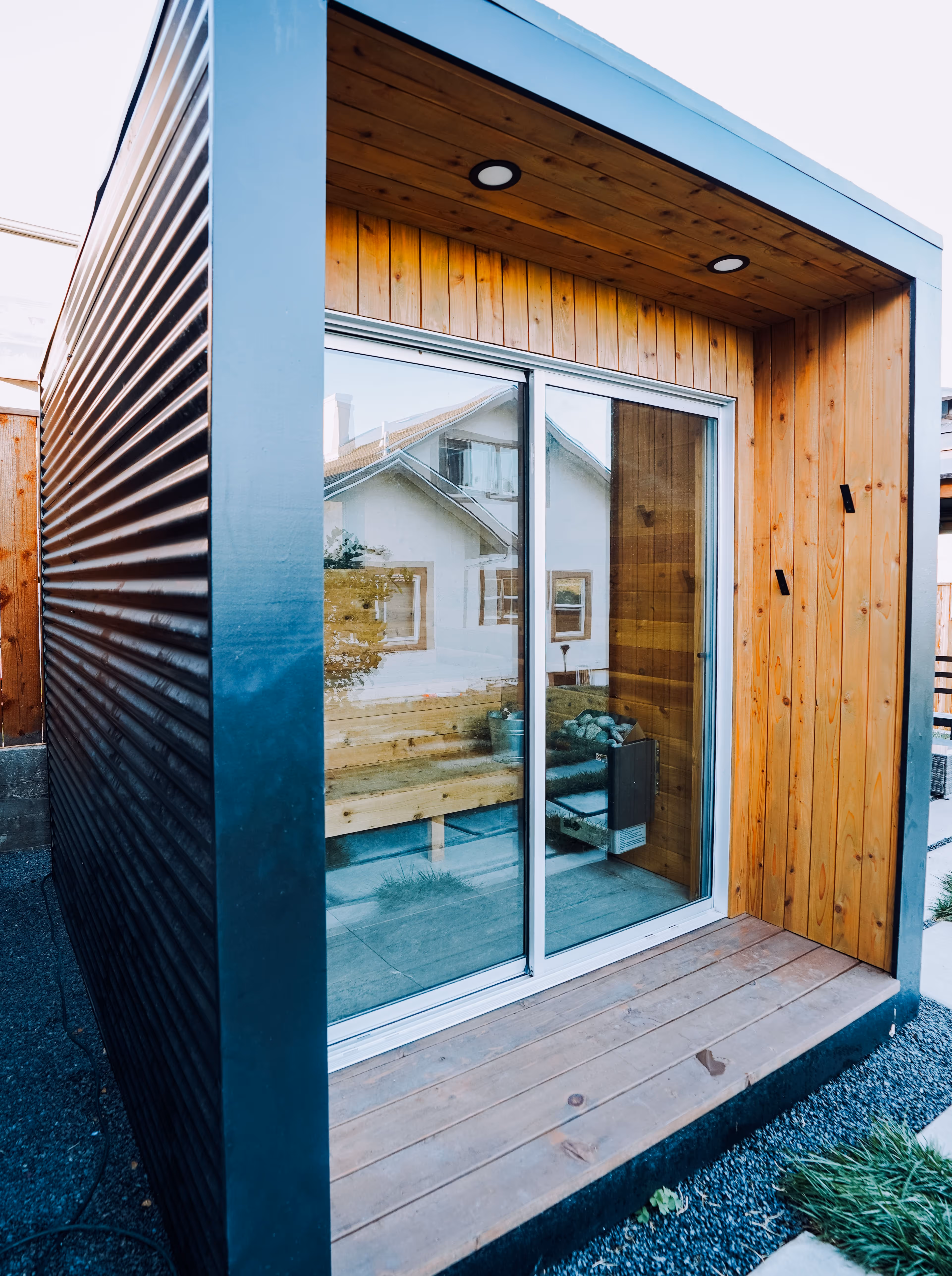 Small modern wooden sauna room with sliding glass doors and metal siding.