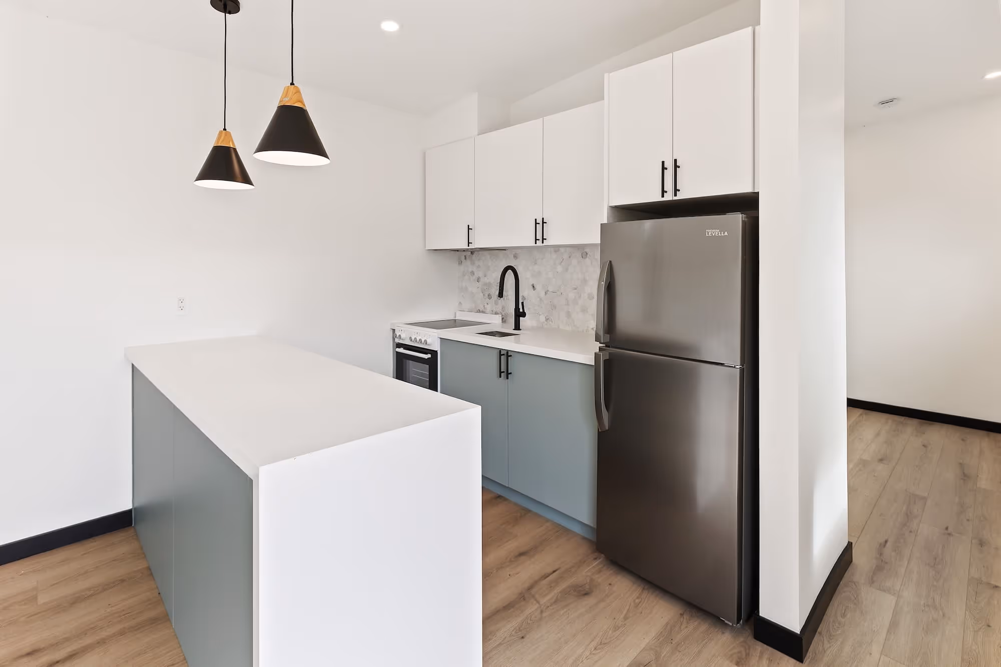 Modern kitchen with white cabinets, gray lower cabinets, stainless steel refrigerator, black faucet, and two black pendant lights over a white island in an ADU.