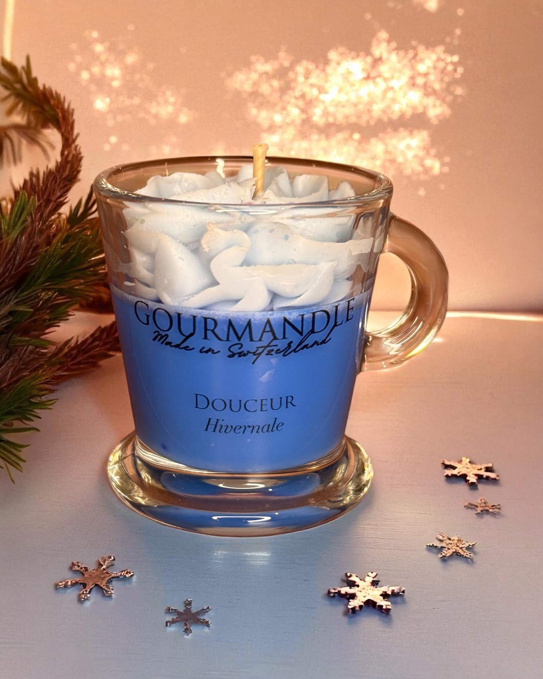 Bougie parfumée "Douceur hivernale" dans un verre transparent marqué "GOURMANDLE, Made in Switzerland". La bougie est recouverte d'une chantilly en cire de couleur bleu pastel.
