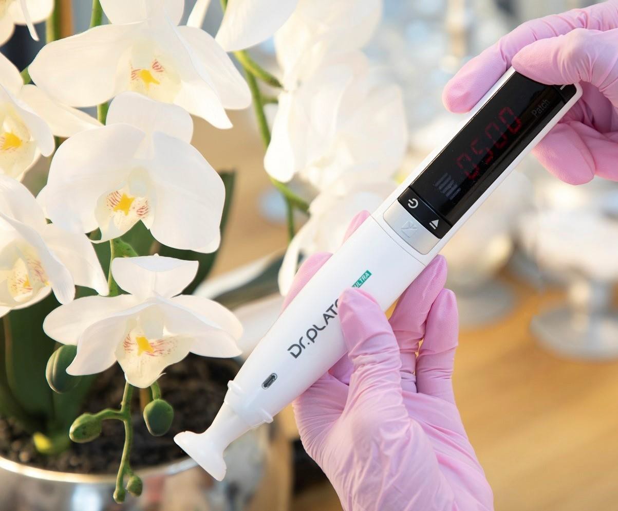 Person mit rosa Handschuhen hält ein digitales Dr. Plato Ultra Messgerät neben weißen Orchideen.
