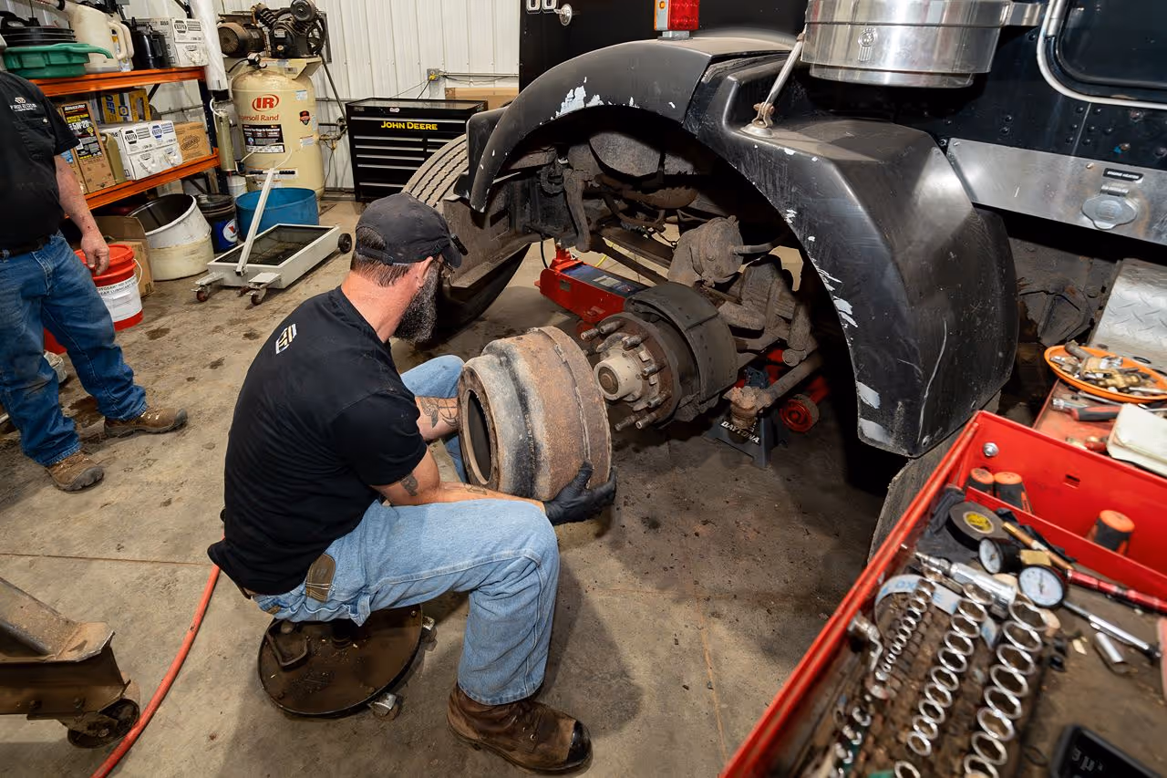 Mechanic removes a worn brake drum from a semi-truck in a repair shop, preparing to service the truck’s air brake system. 
