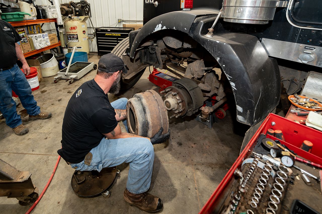 Mechanic removes a worn brake drum from a semi-truck in a repair shop, preparing to service the truck’s air brake system. 