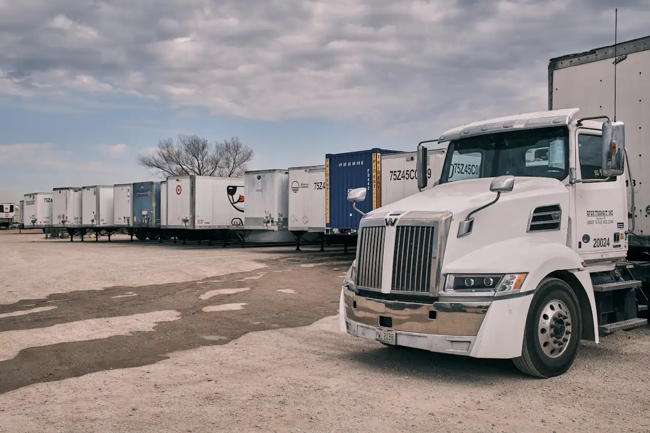 Fleet maintenance with a heavy-duty semi truck parked beside a row of commercial trailers in a fleet yard.