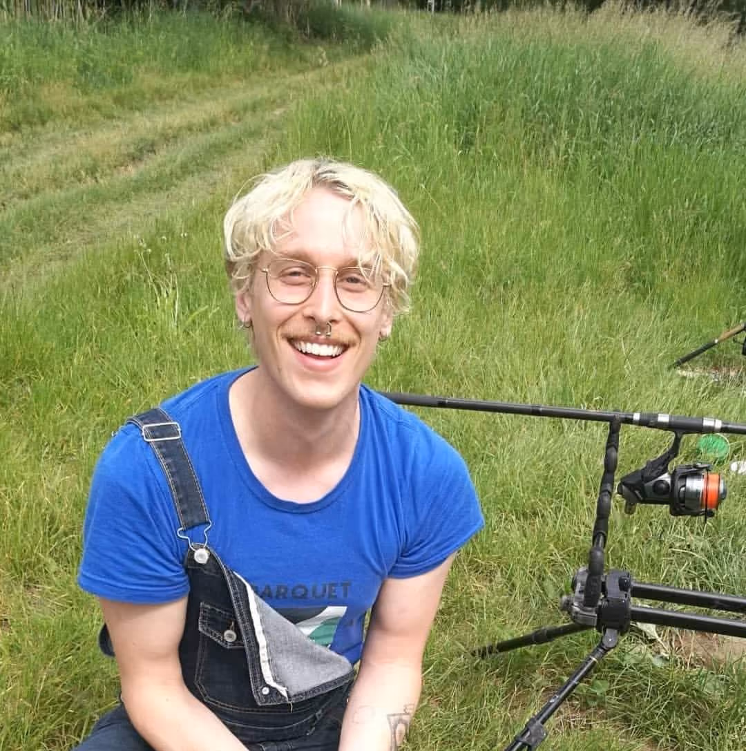 A man holding a fish and smiling in a grassy field