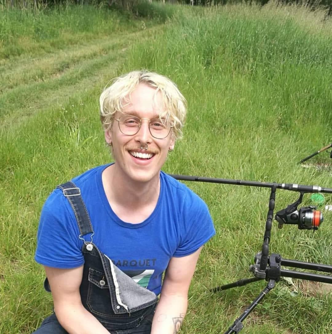 A man holding a fish and smiling in a grassy field
