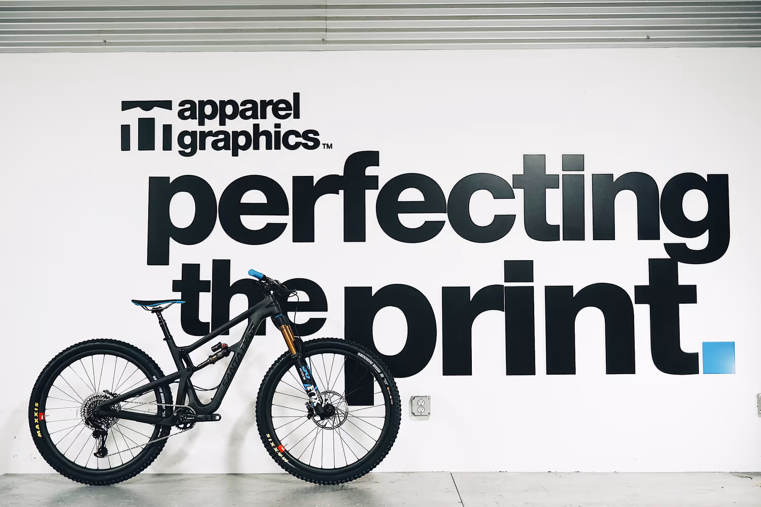 A wall mural displaying the Apparel Graphics logo with "Perfecting the Print" in bold lettering