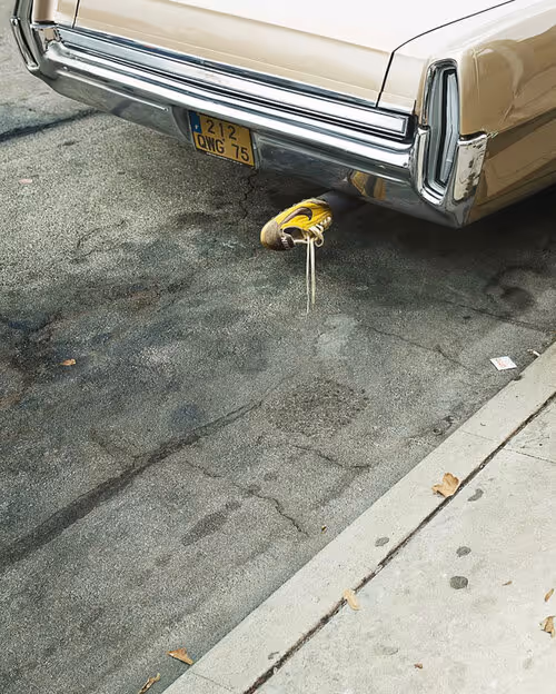 Rear bumper of vintage cream-colored car with yellow sneaker beneath it