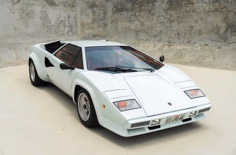 White Lamborghini Countach sports car on light beige floor against textured gray wall