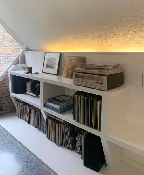 White shelving unit under sloped ceiling with vintage record player and vinyl collection