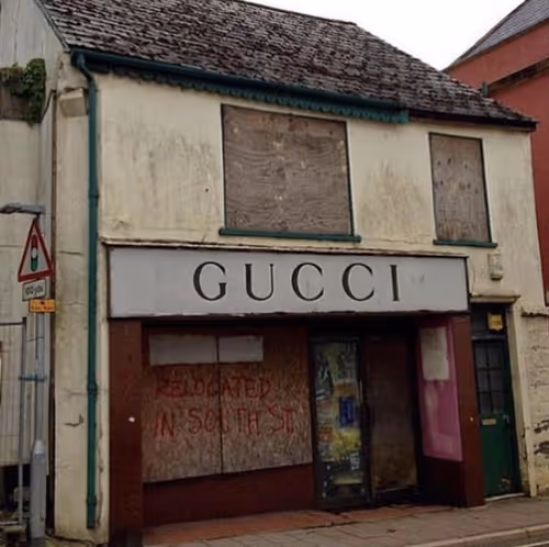 Abandoned Gucci storefront with boarded windows and 'RELOCATED IN SOUTH ST' spray-painted on plywood