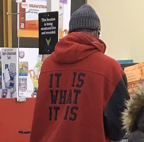 Person in red hoodie with 'IT IS WHAT IT IS' printed on back