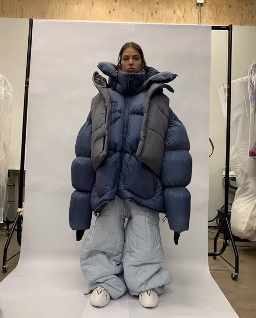 Model wearing oversized blue and gray puffer jacket with matching pants against white backdrop
