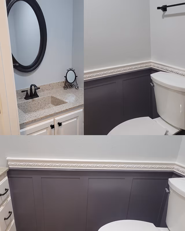 Modern bathroom corner with white toilet, dark gray wainscoting, white molded chair rail, granite countertop sink with black faucet, and round black-framed mirror.