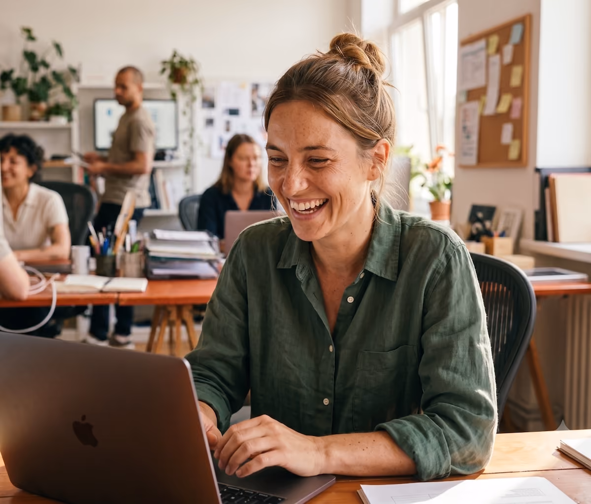 Femme souriante travaillant sur un ordinateur portable dans un bureau lumineux et partagé.