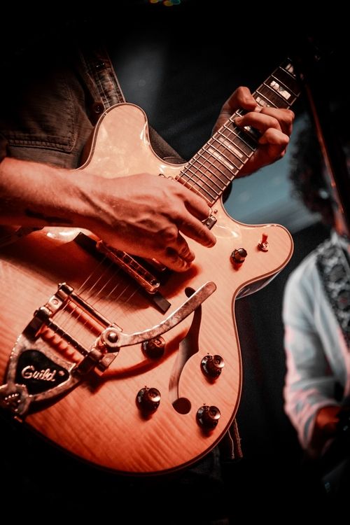 Close-up of hands playing a natural wood finish Guild electric guitar on stage.