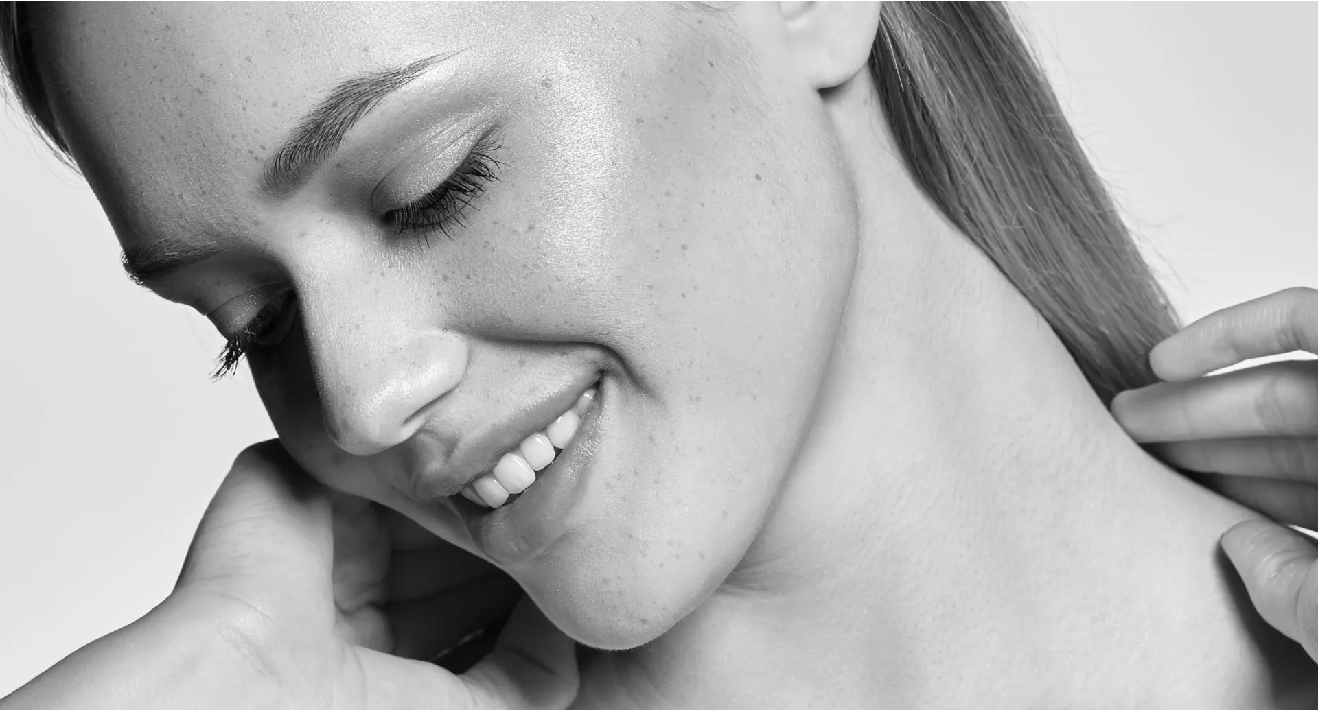 A smiling woman, touching her neck.
