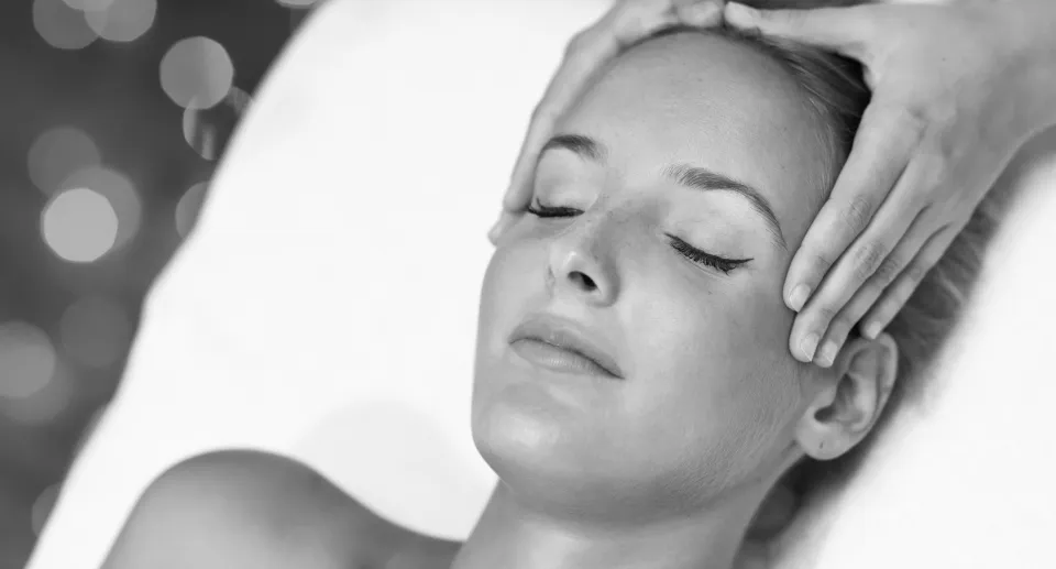 Woman with closed eyes receiving a gentle head massage with hands on sides of her face.