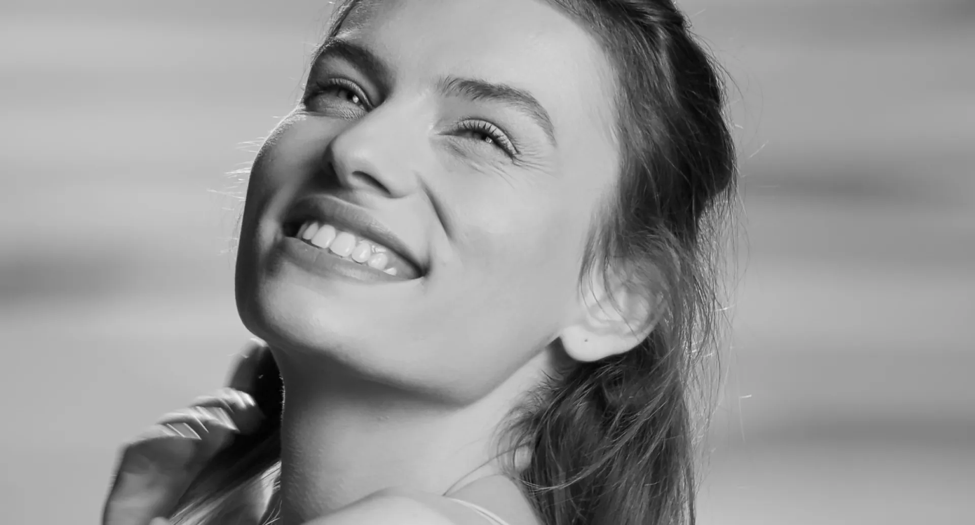 Close-up of a woman smiling and looking upward in black and white.