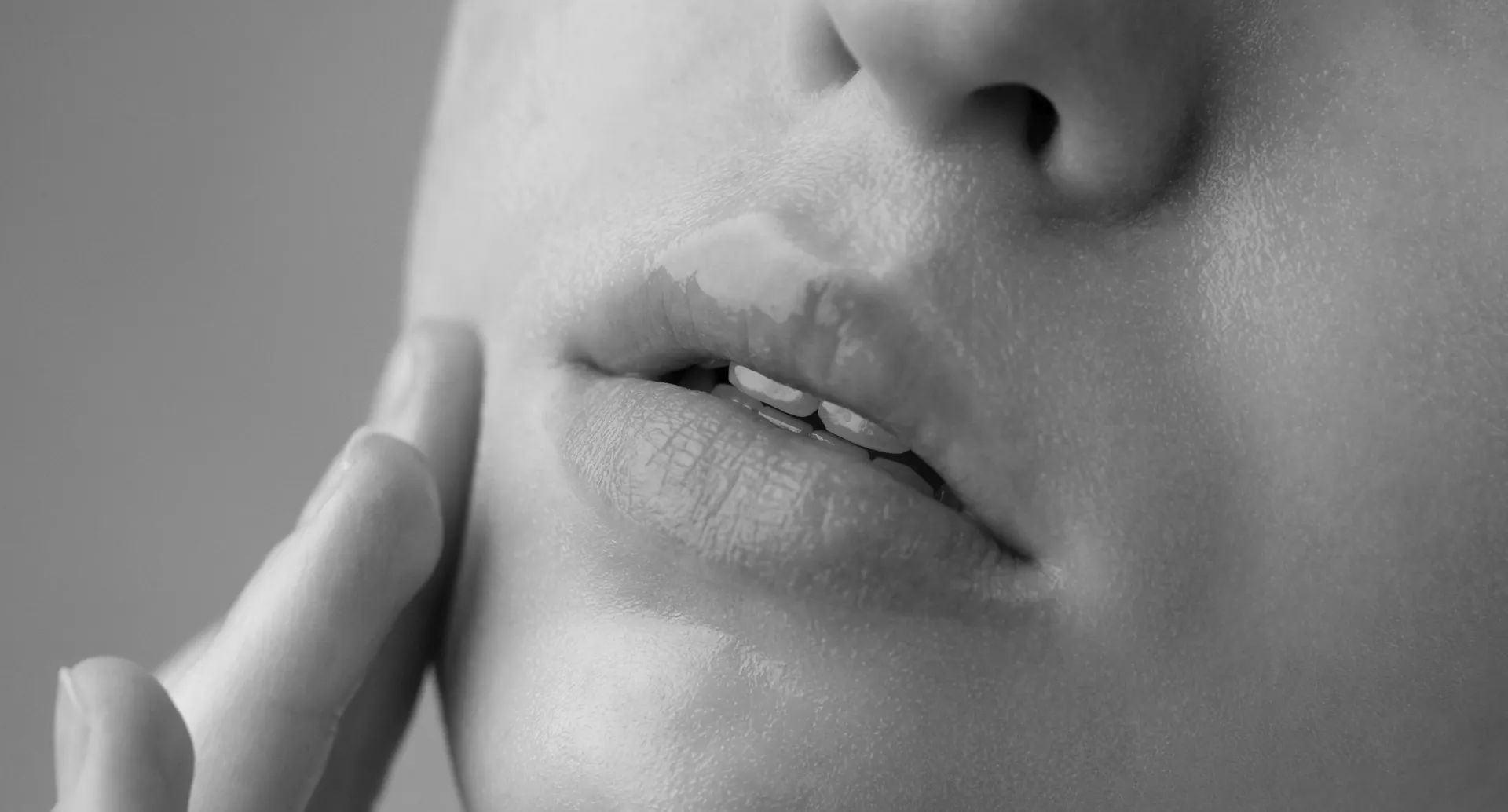 Close-up of a person's lips slightly parted with a finger touching the cheek, in black and white.