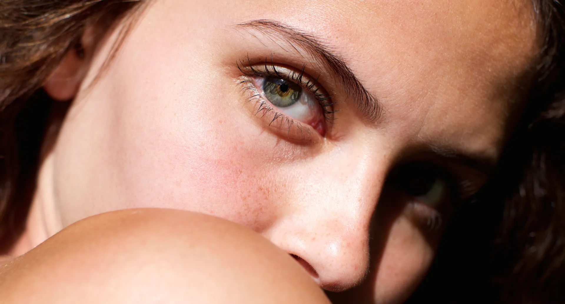 Close-up of a person's face focusing on a green eye, eyebrow, and shoulder.