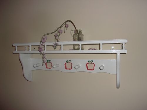 a small glass vase holds a dried bleeding heart flower and sits on a white wall shelf that has apple cut outs on it painted red and green