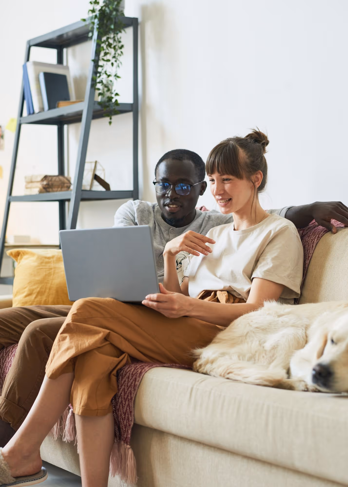 Couple sitting on couch with dog, viewing rental options on laptop