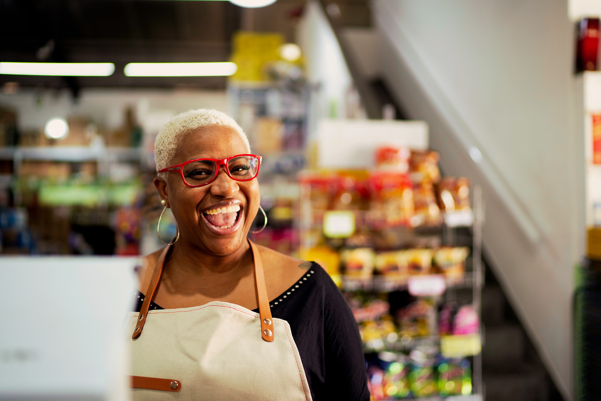 Dona de um pequeno mercado sorrindo pra a câmera