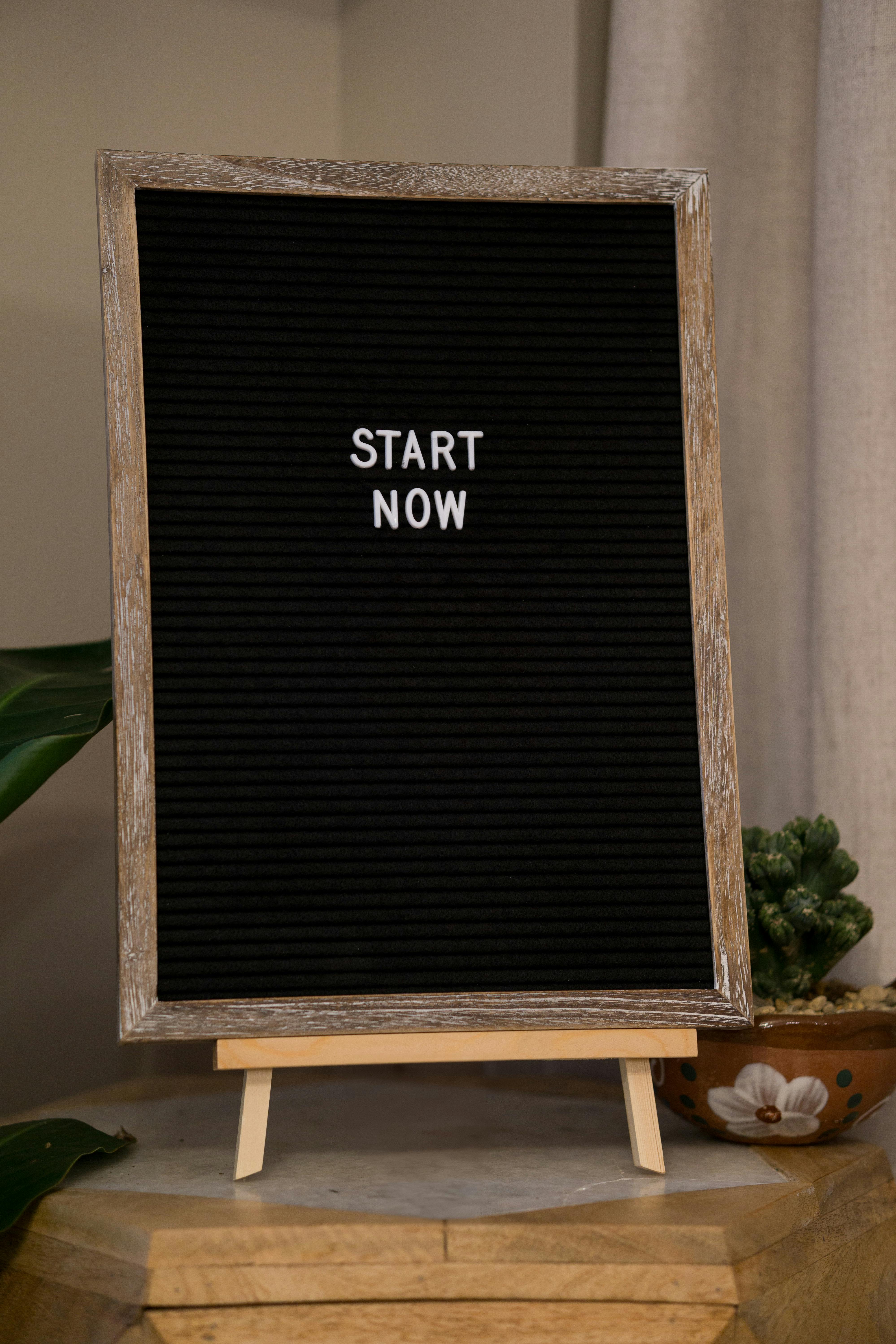 Black felt letter board with wooden frame on a small wooden easel displaying the message 'START NOW'.