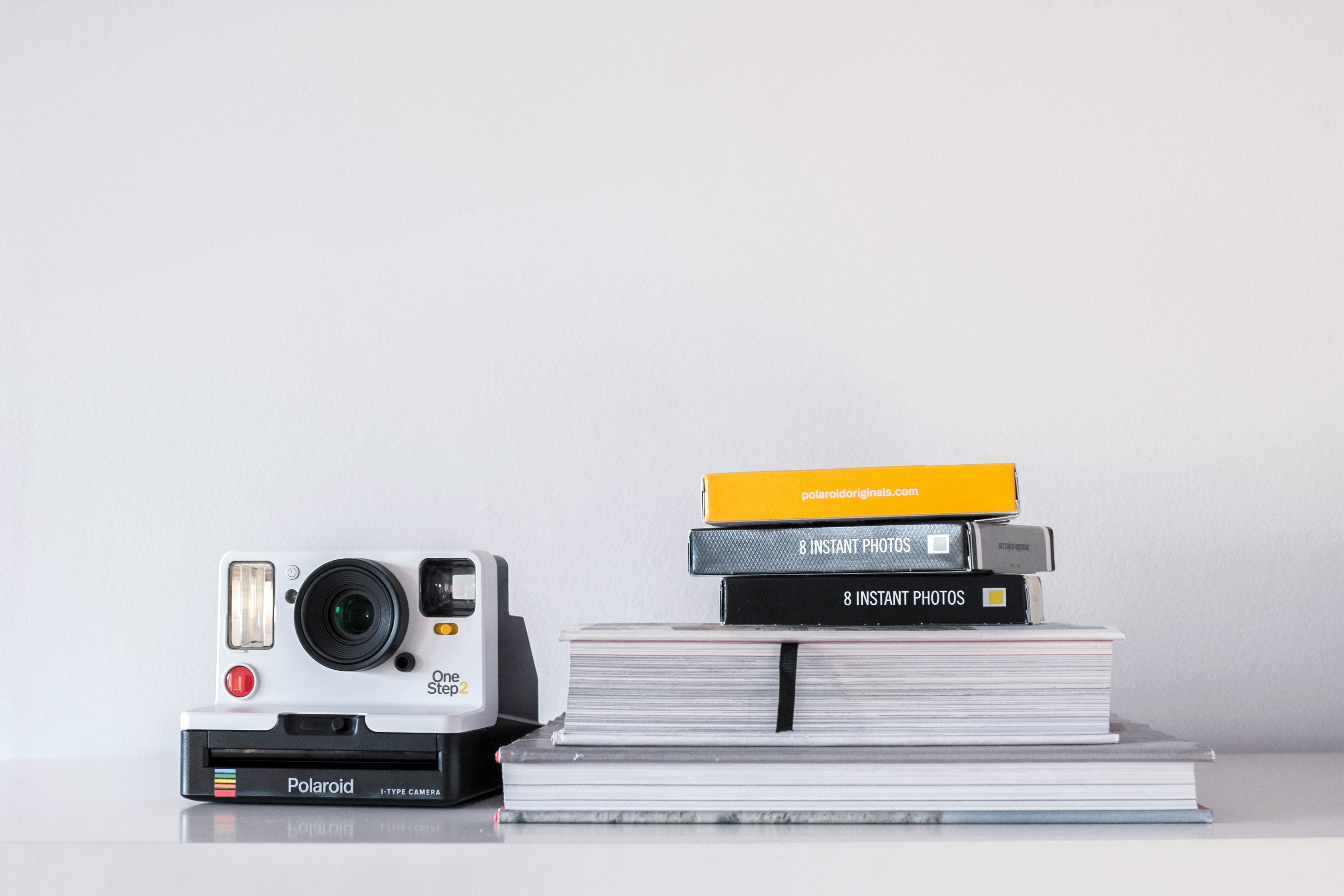Polaroid OneStep 2 camera next to a stack of books and photo film boxes on a white surface.