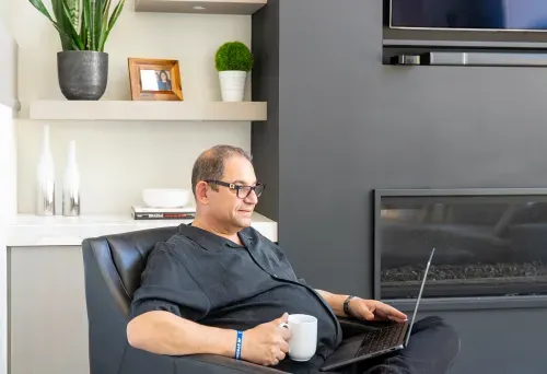 Homeowner on laptop sitting by living room fireplace
