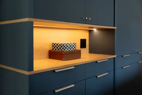Close up of navy blue painted cabinets with under-cabinet lighting and decorative boxes stacked on countertop