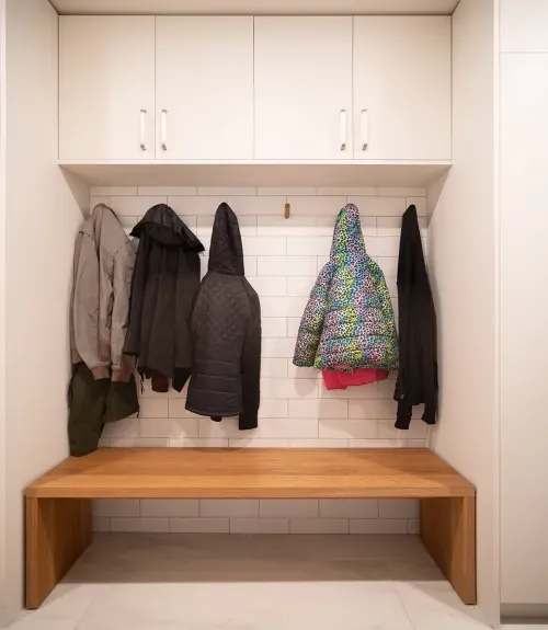 Built in mudroom seating bench and cabinets with coats hanging on wall hooks