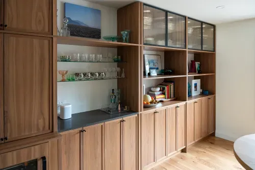 Angled view of wooden kitchen cabinetry along back wall, holds decorative objects and glassware