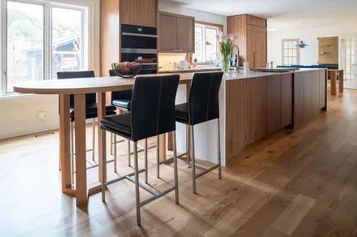 View of length of kitchen island with stylish velvet bar stools and wooden cabinets