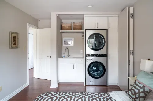 Spacious room with built in cabinetry holding stacked washer and dryer, laundry tub