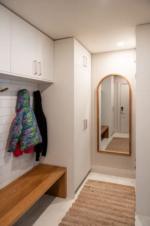 Mudroom with mirror hanging on one wall, built-in wooden bench and coat hooks along another
