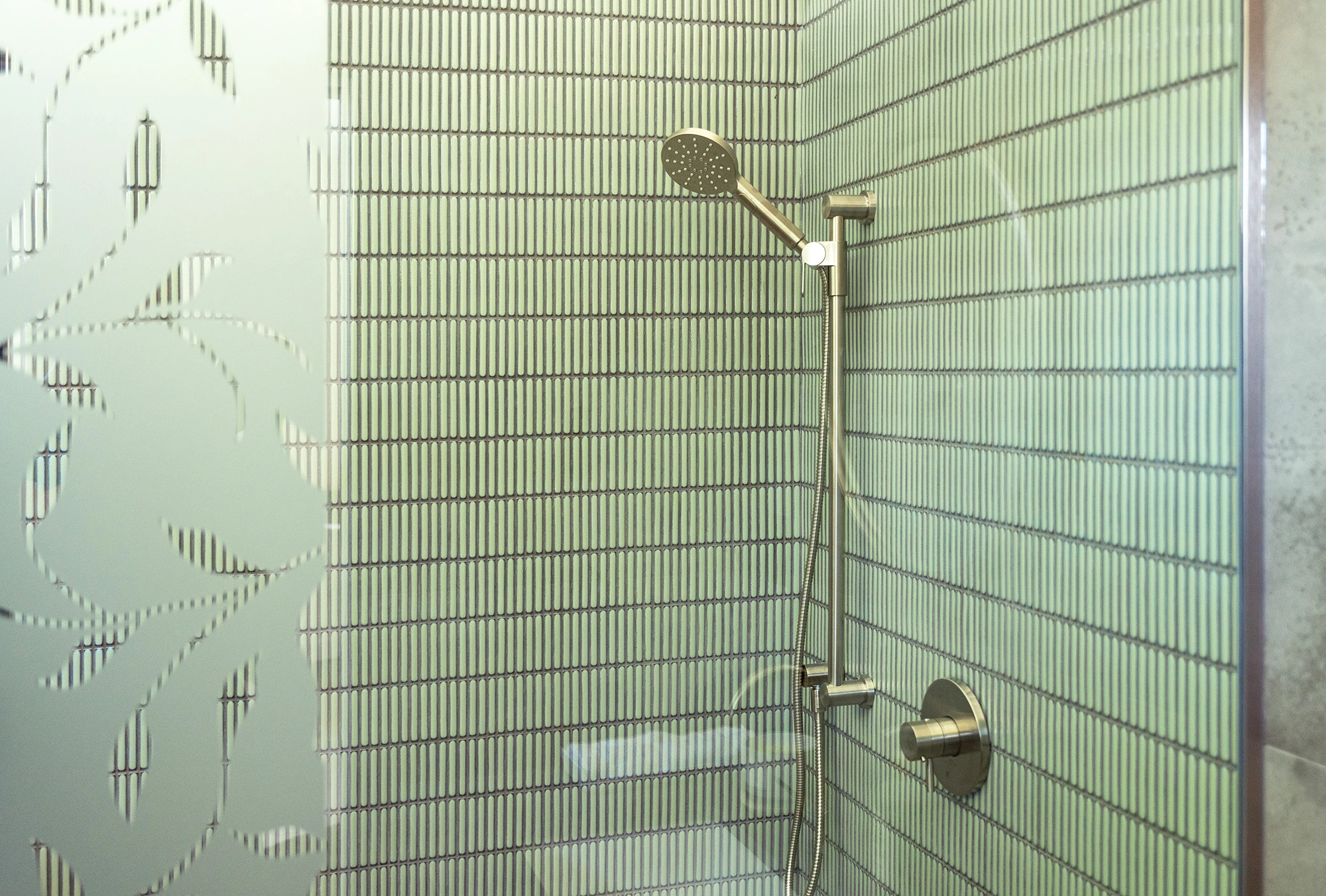 Green tiled walk-in shower encased in glass walls