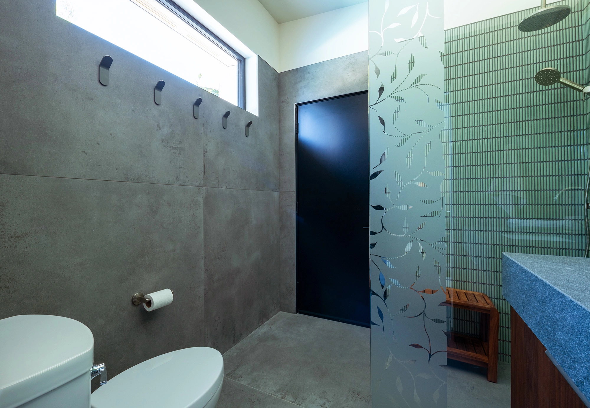 Bathroom space with glass and tile shower, large rectangular window, wooden cabinetry, and stone walls