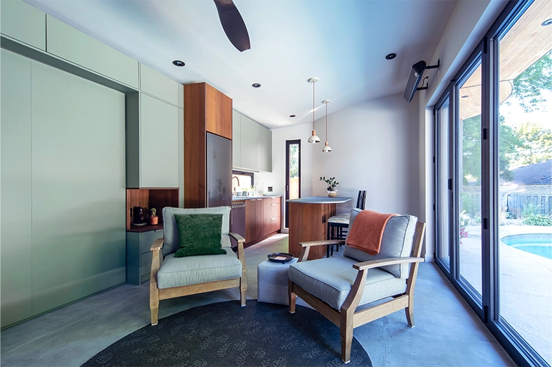 Pool house seating area with two beachy armchairs, modern kitchenette can be seen in background
