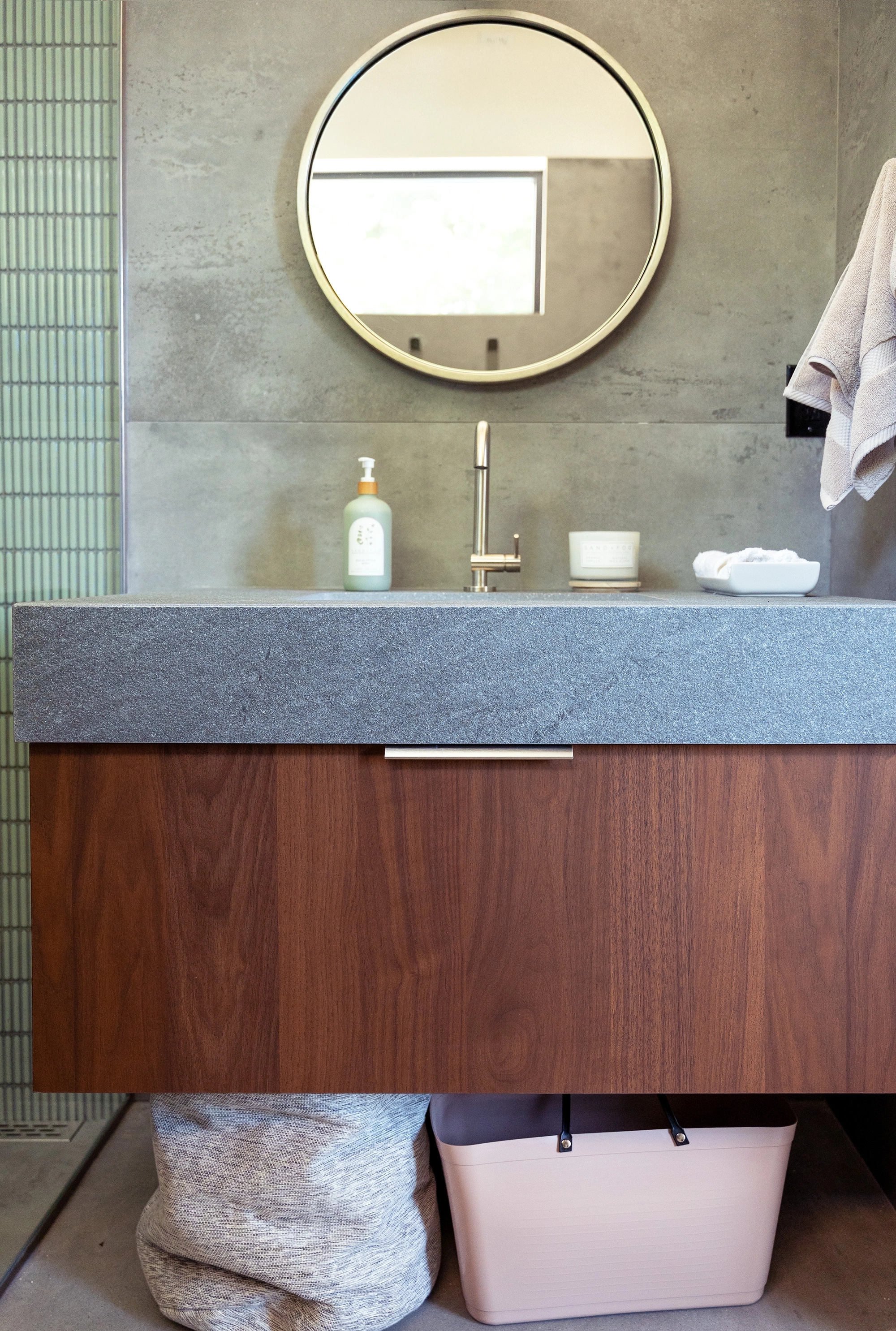Bathroom vanity with wooden cabinetry, stone countertops and gold circular mirror