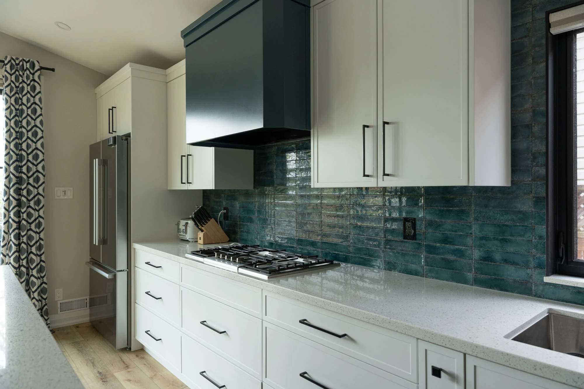 White kitchen cabinetry along back of wall with blue range hood and backsplash