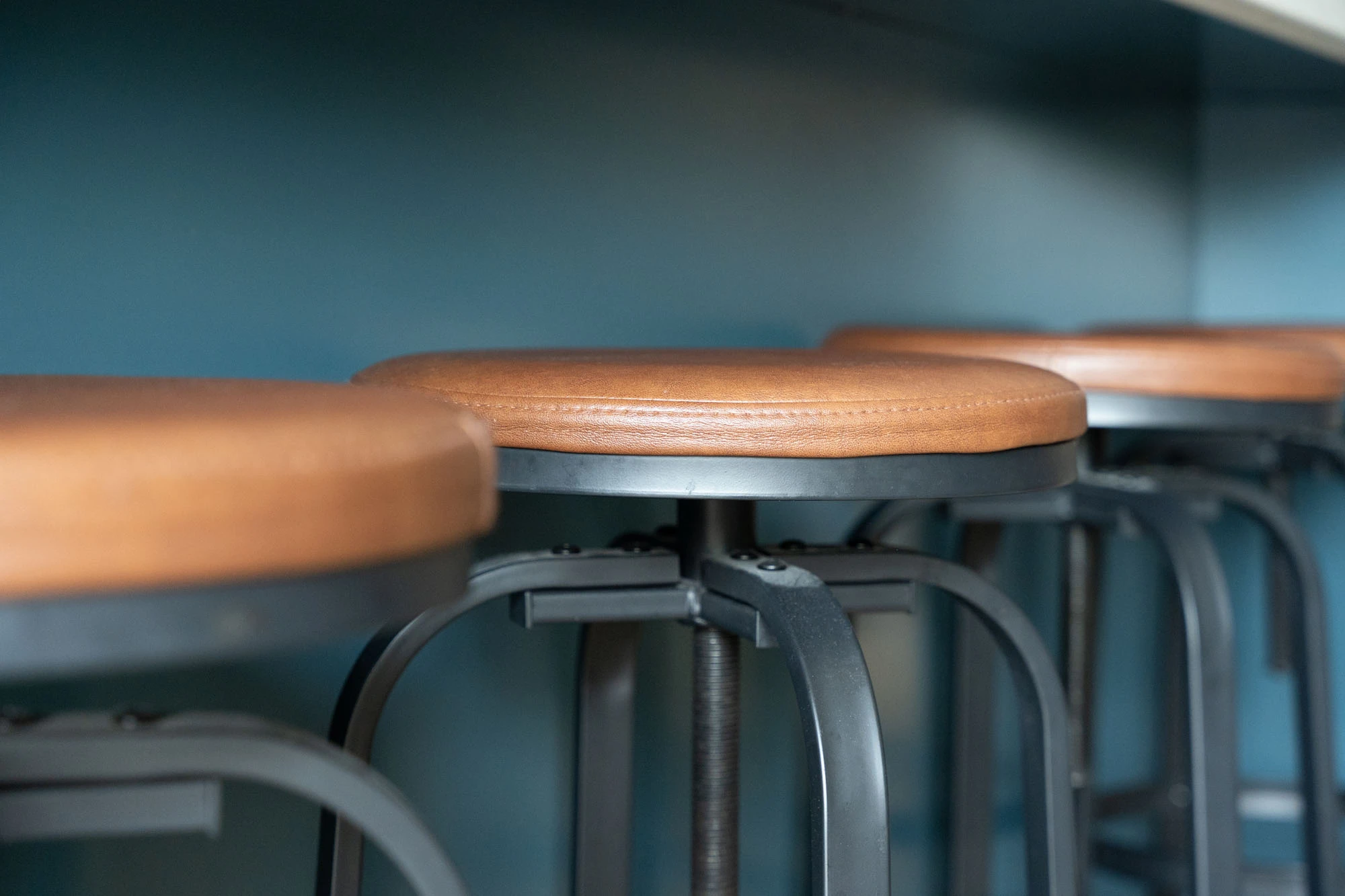 Close up of leather-upholstered kitchen stools lined up against blue kitchen island