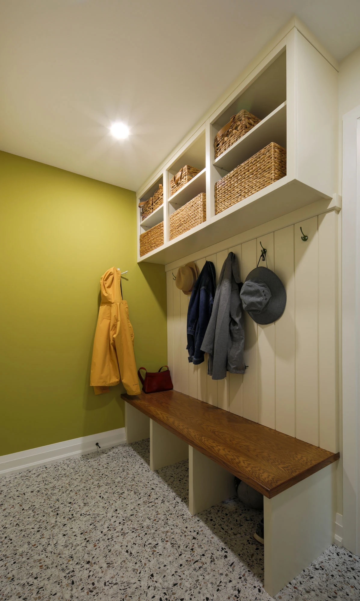 Mudroom area with lime green walls, white wooden cabinetry, coat hooks, and bench.
