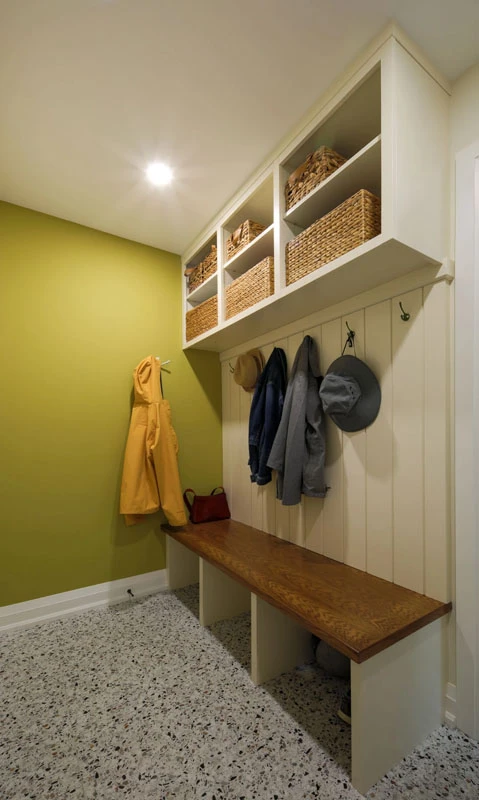 Mudroom area with lime green walls, white wooden cabinetry, coat hooks, and bench.