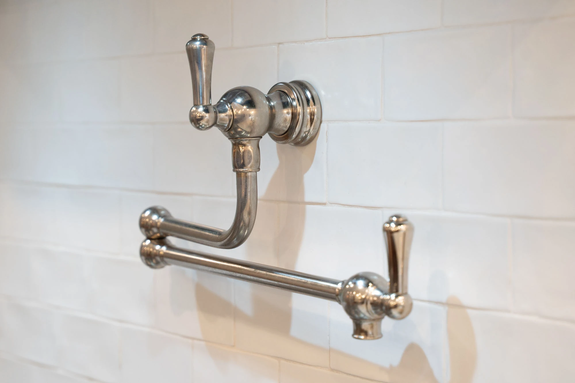 Close up of pot filler faucet installed on white tile backsplash on stovetop wall