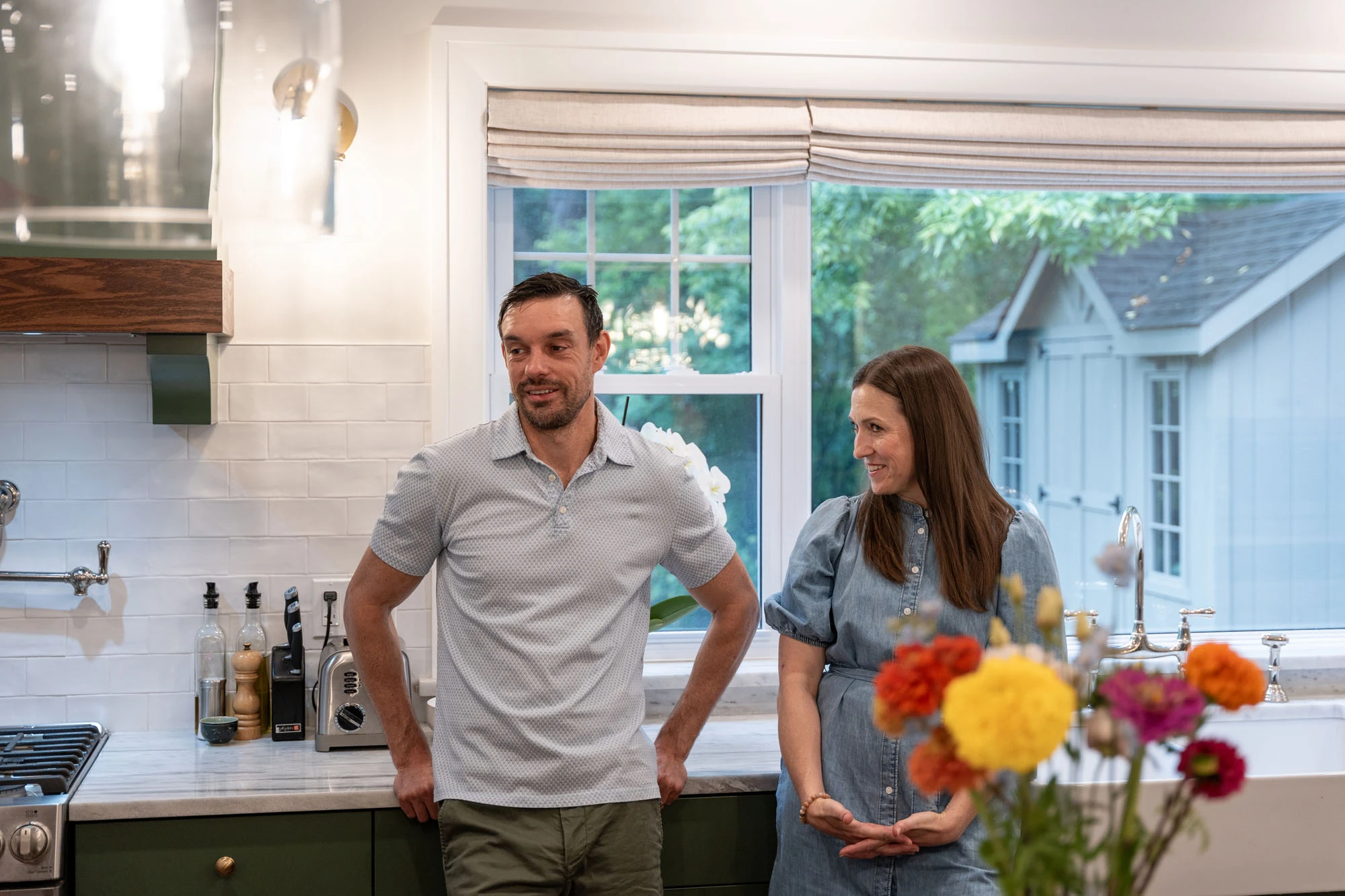 Smiling homeowners stand together leaning against granite countertops near kitchen sink